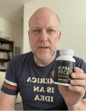 Man in a t-shirt holding AlphaRock capsules at home